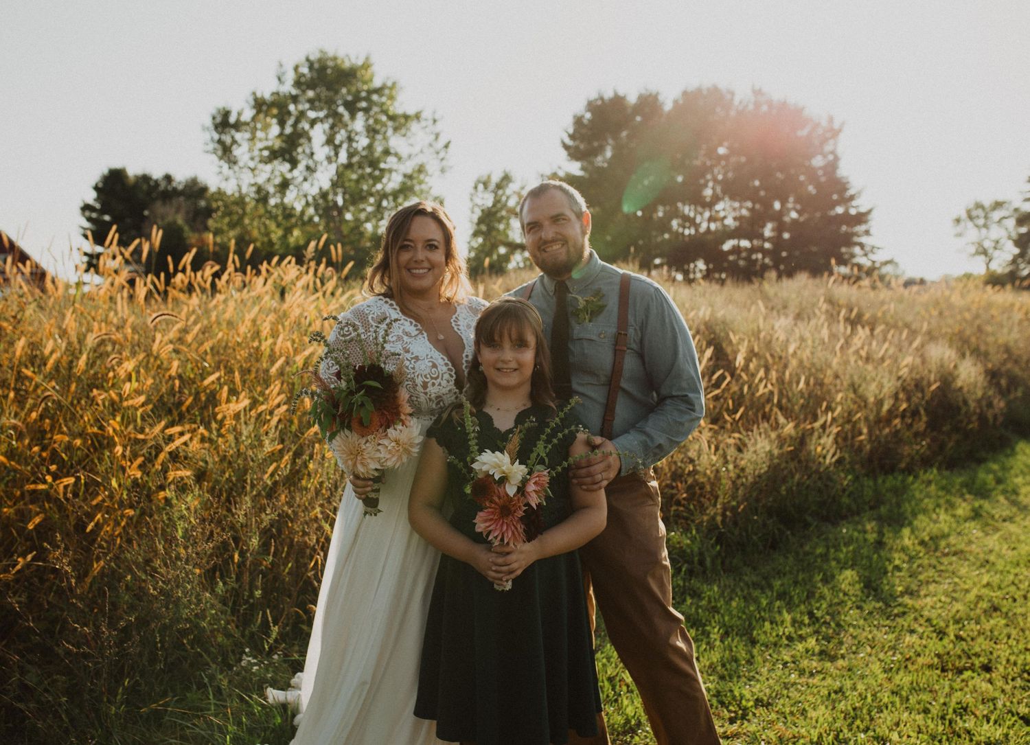 Wedding couple and guests share intimate moments in a golden sunlit field during sunset.