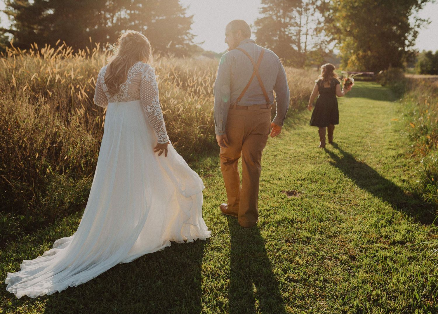 Silhouettes of wedding party members walking through a sun-drenched field at dusk.