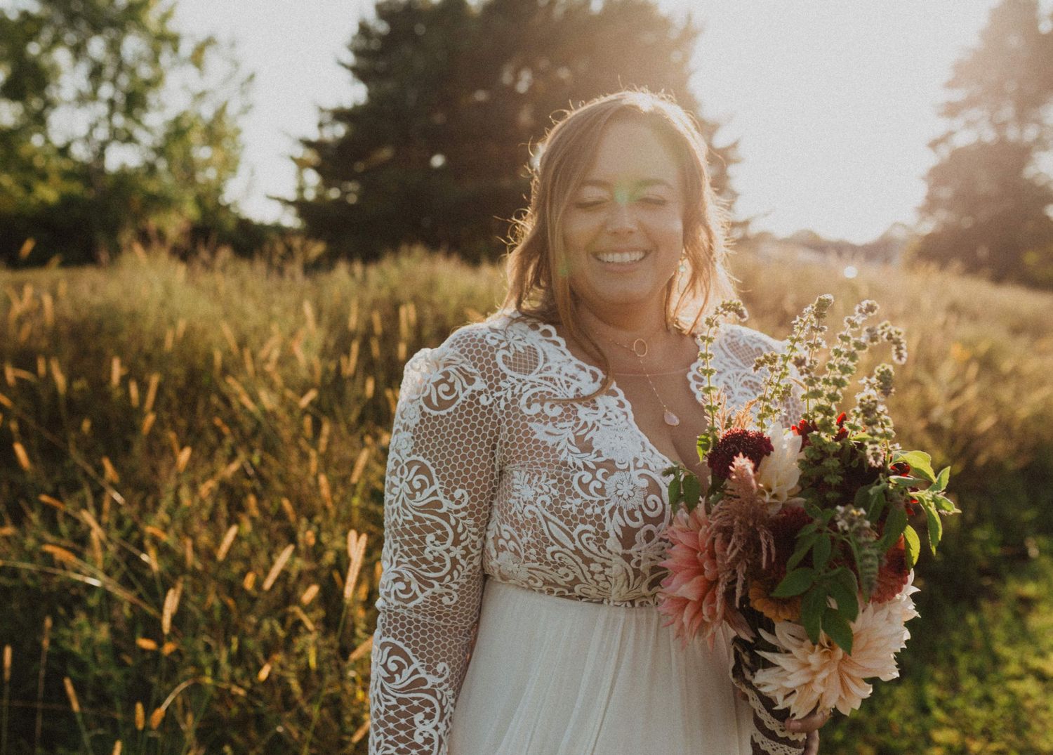 Close-up portrait of a bride holding a bouquet in golden sunlight with lace dress details.