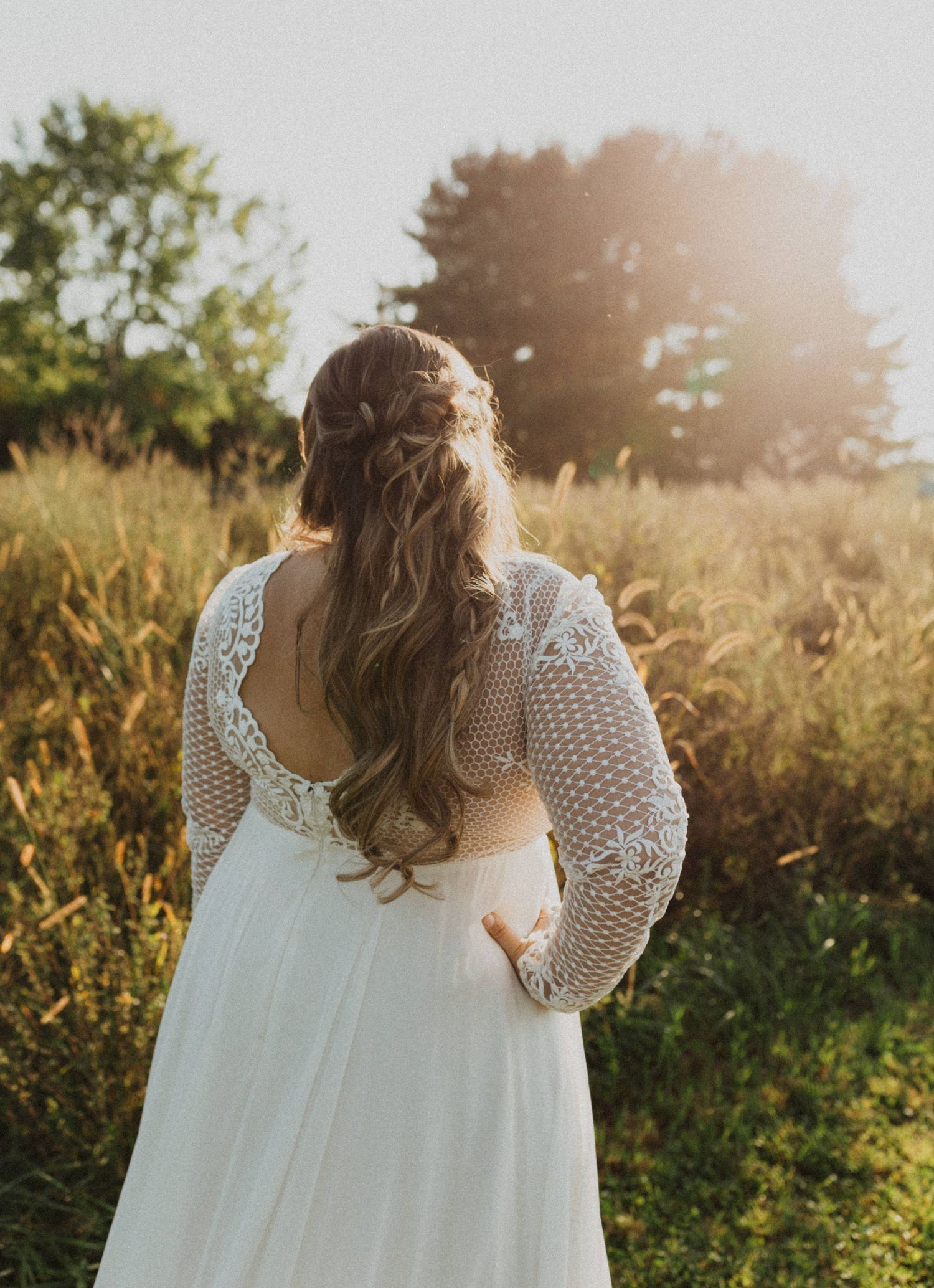 Back view of an elegant white lace wedding dress photographed in a rustic outdoor setting.