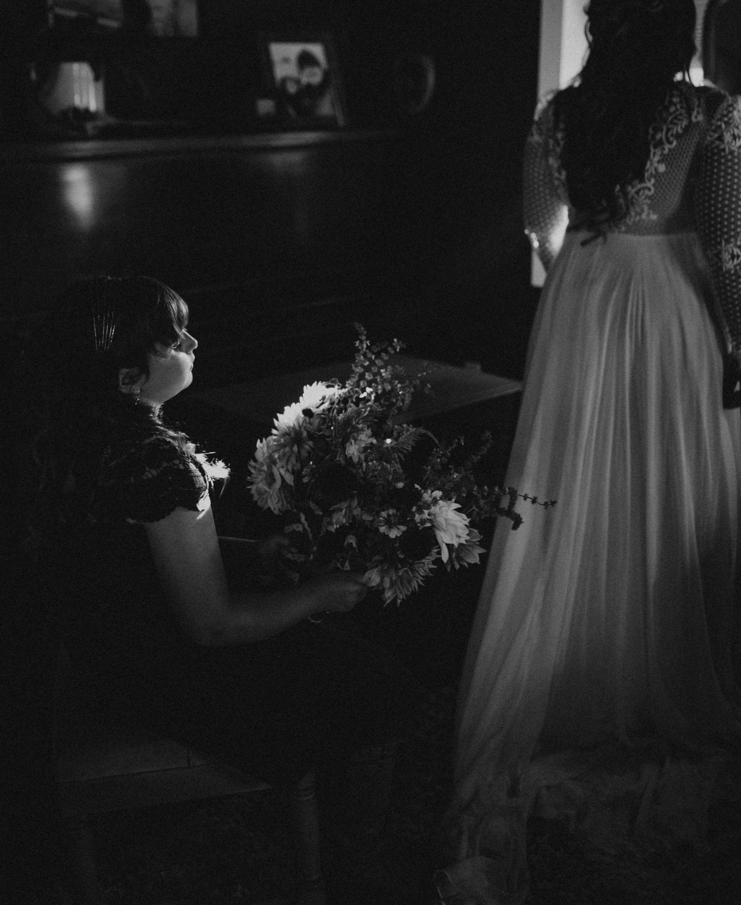 Moody black and white photo showing flowing white dress details in dark interior lighting.