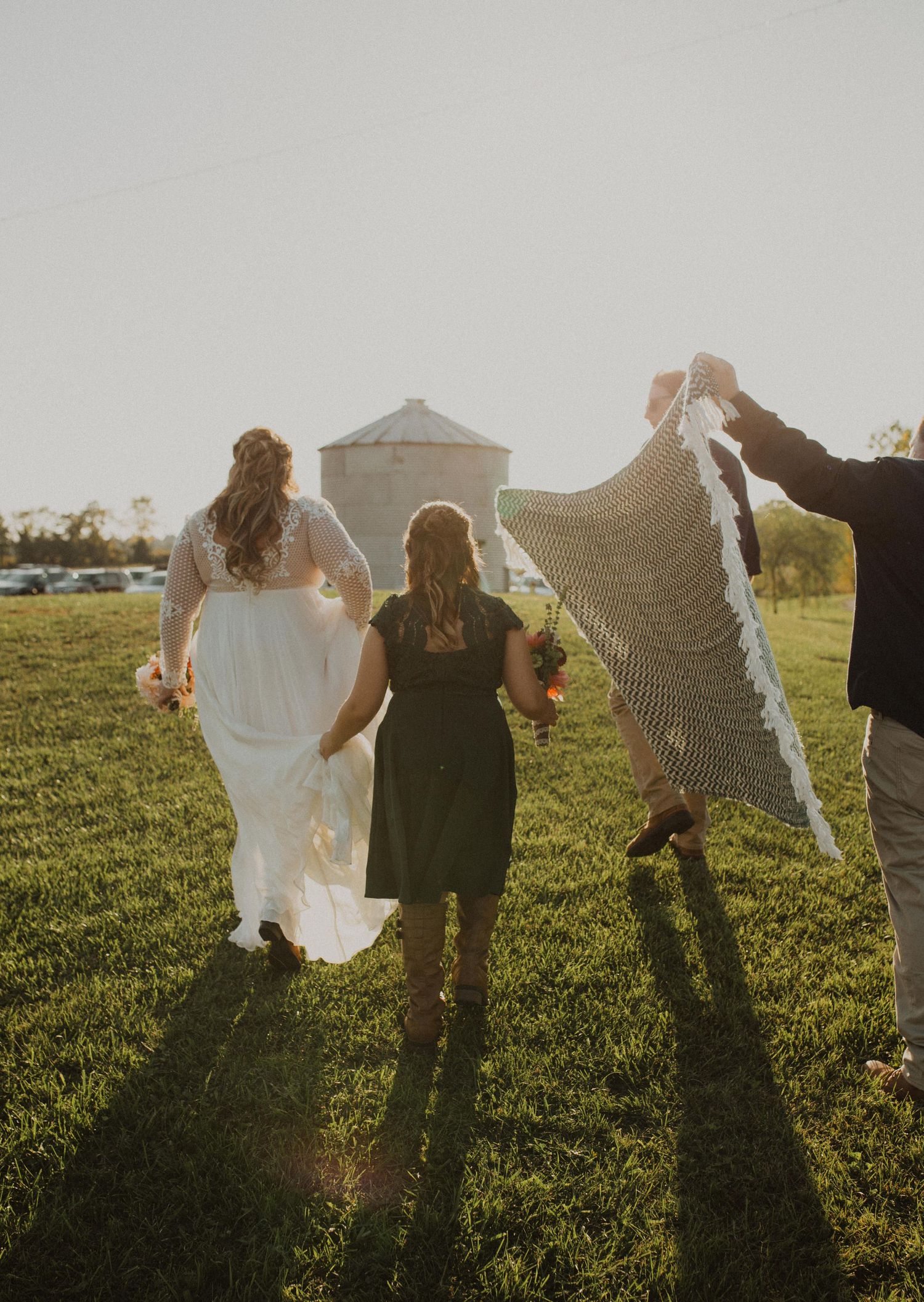 Silhouettes of people holding up fabric against the setting sun in a grassy field.