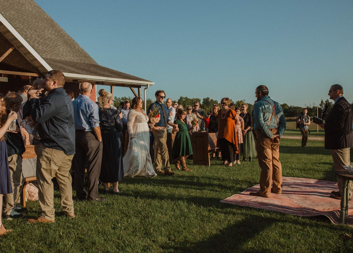 Wedding guests gathered outdoors on a grassy lawn during golden hour.