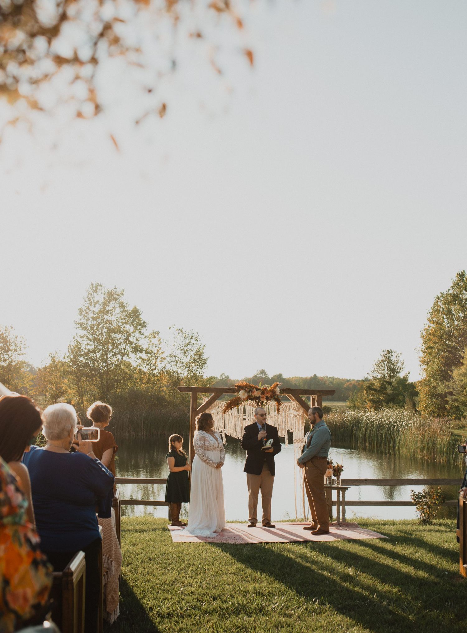 Outdoor wedding ceremony by a lake during sunset with guests in attendance.