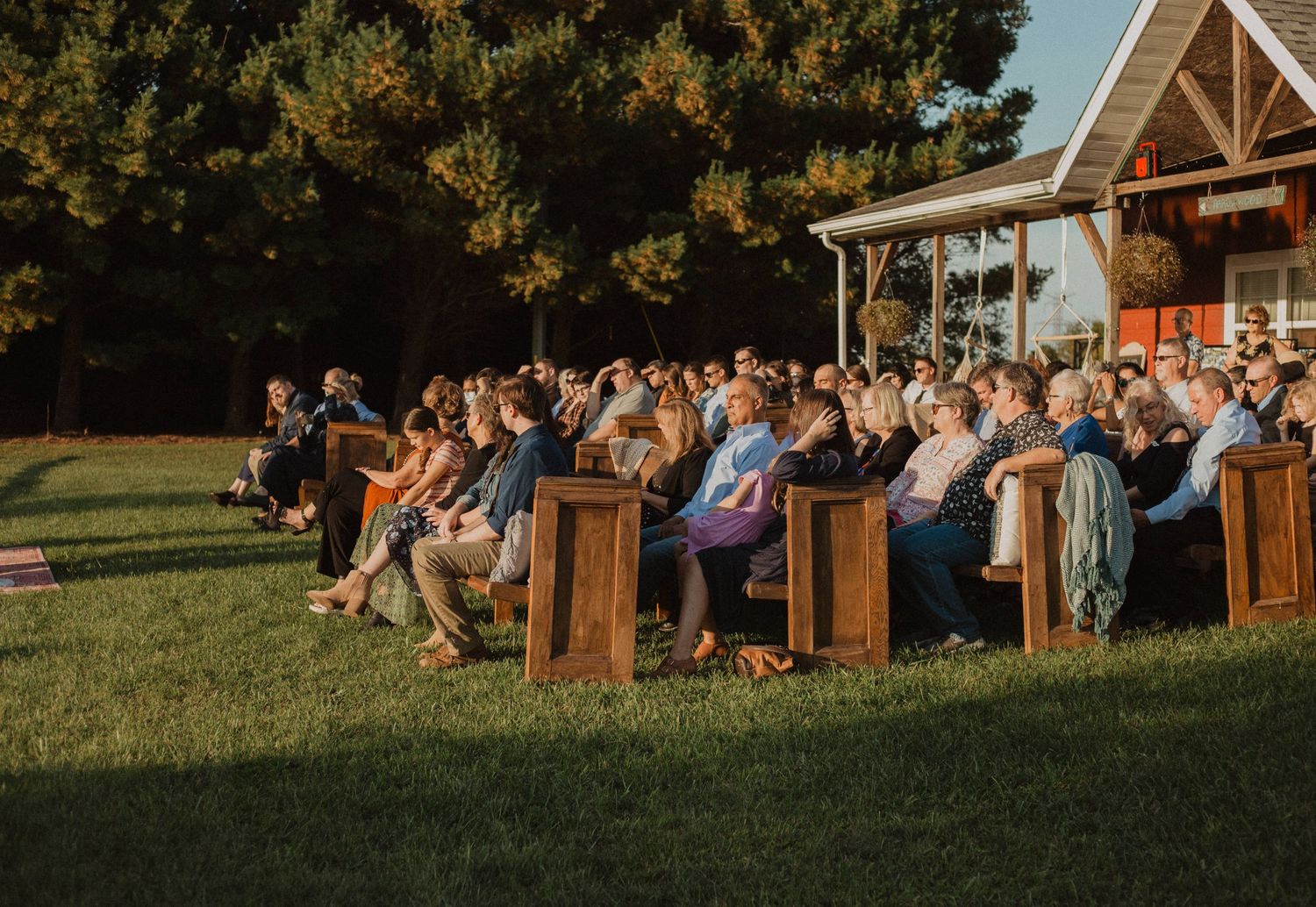 Wedding guests seated on wooden benches during outdoor ceremony.