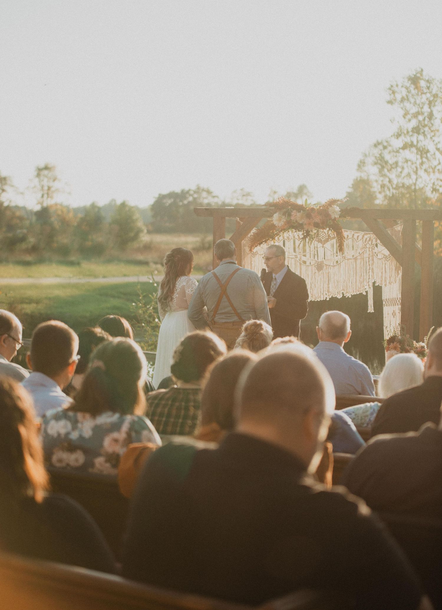 Sunset wedding ceremony with guests seated on wooden benches watching proceedings by the water.