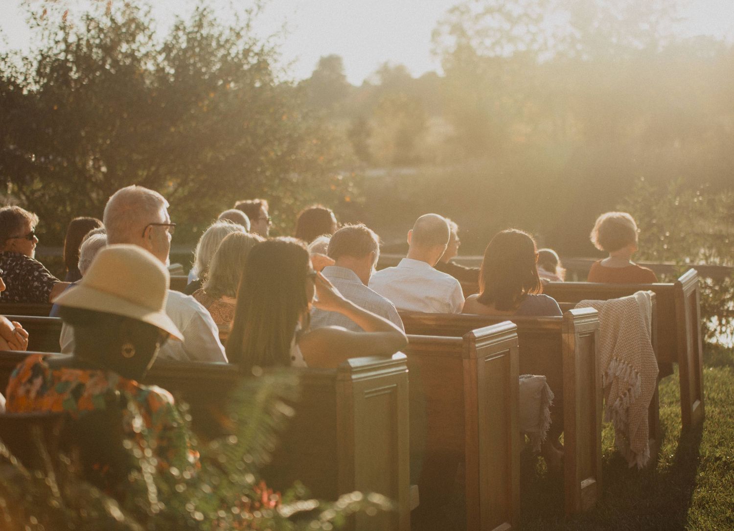 Wedding guests seated on rustic wooden benches during golden hour outdoor ceremony.