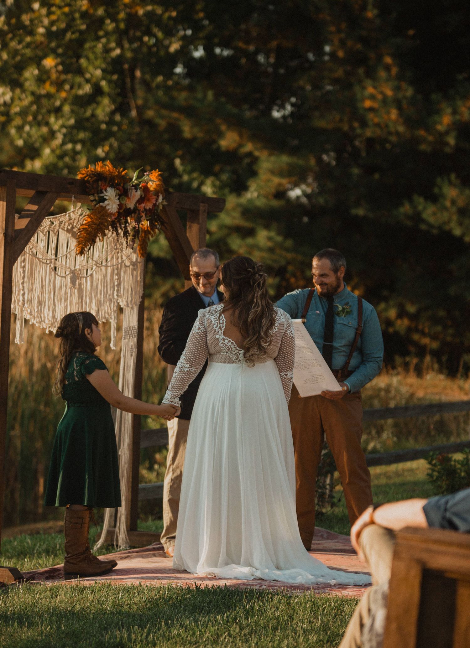 Rustic outdoor wedding ceremony with macrame backdrop and wooden arch decorations.