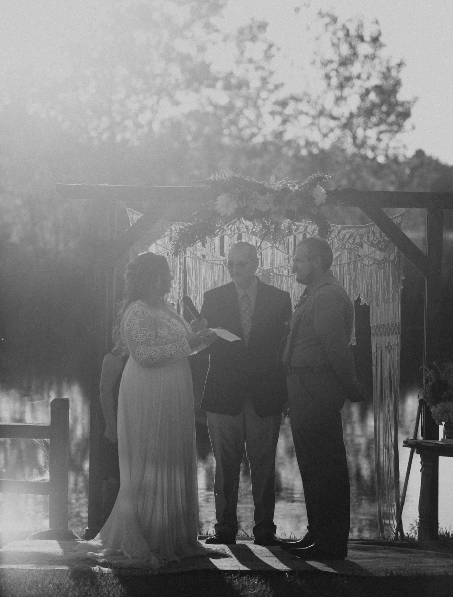 A black and white photo captures a wedding ceremony moment under a decorated wooden arch.