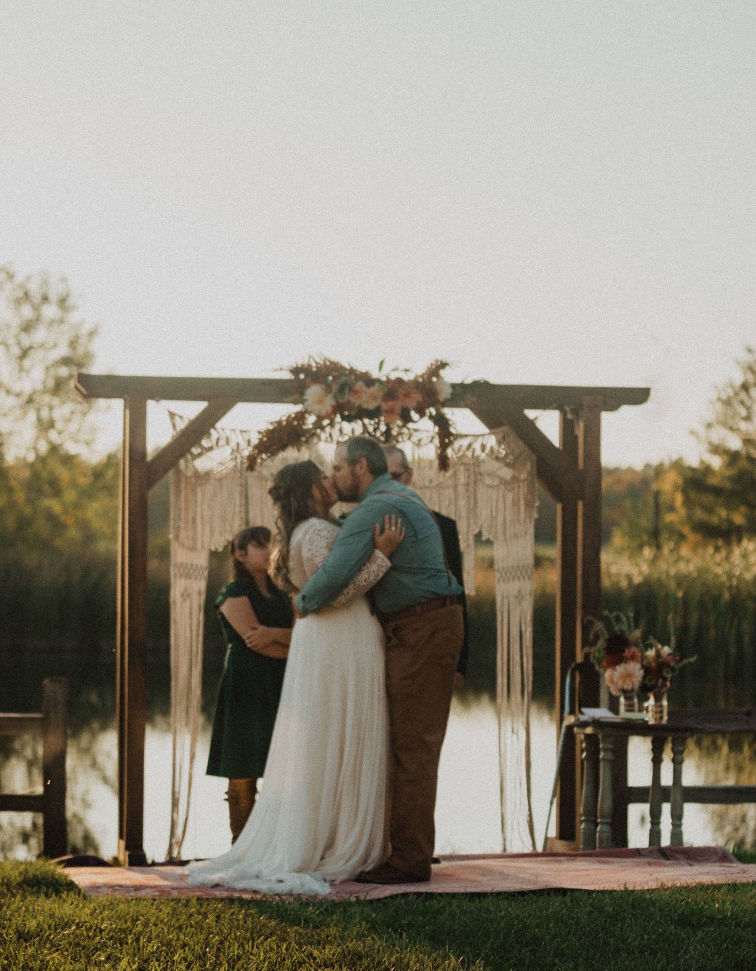 An emotional group embrace concludes the wedding ceremony under a macrame-decorated arch.