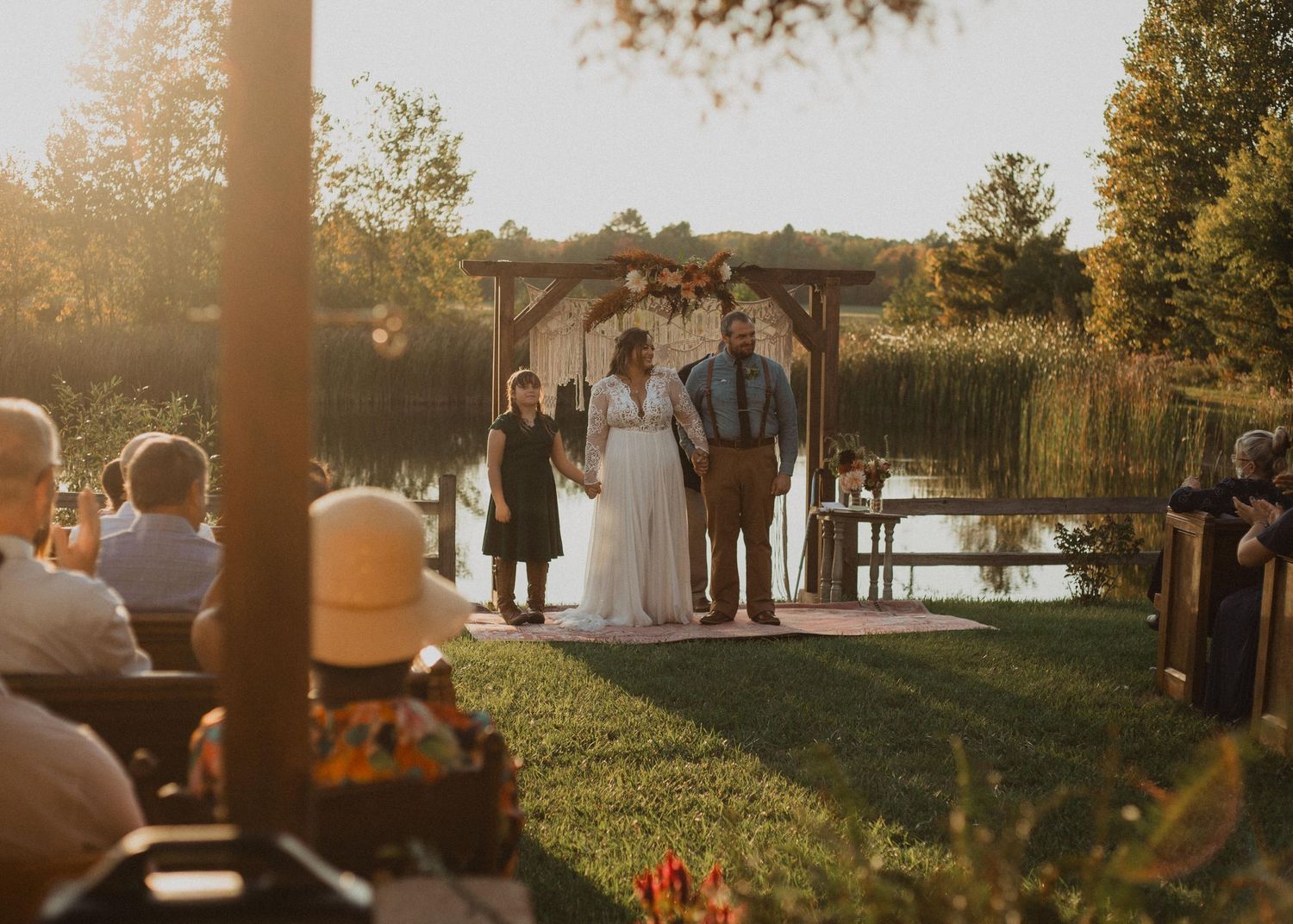 A waterfront wedding ceremony with guests watching from wooden benches during golden hour.