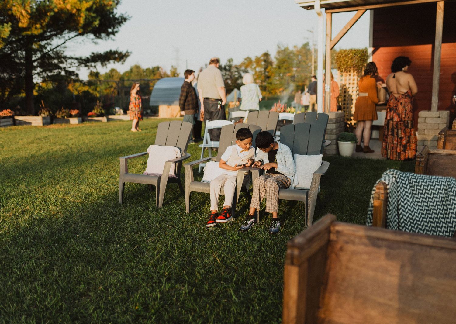 Outdoor wedding reception setup with tables and chairs on a grassy lawn at sunset.