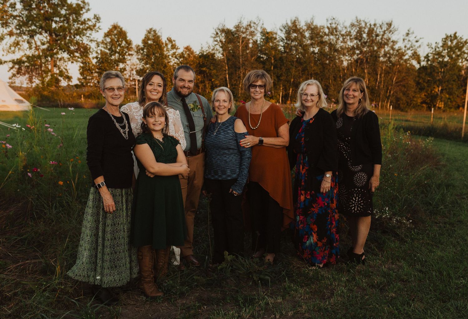 Wedding party poses together outdoors at sunset near a rustic barn.