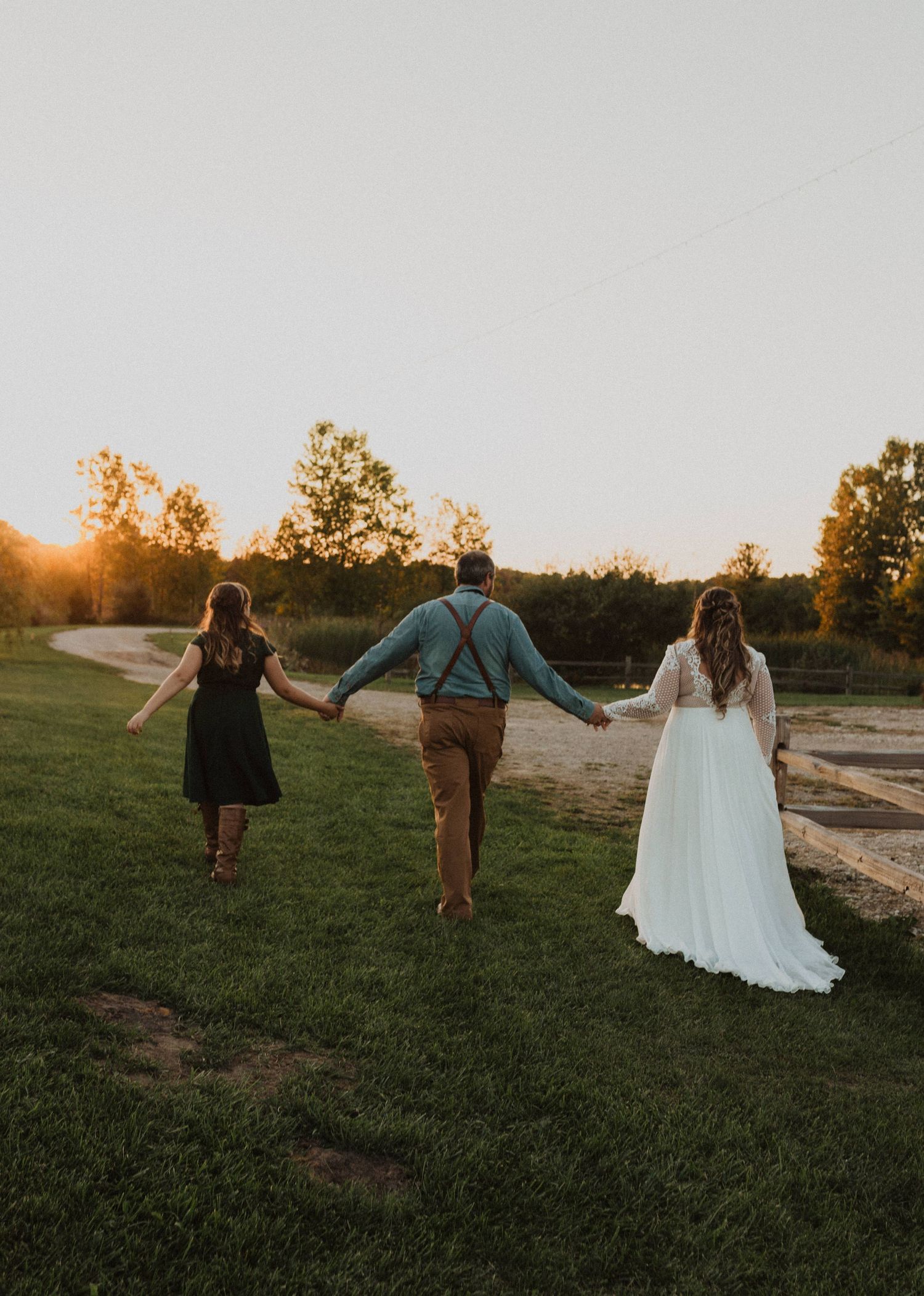 Wedding party members walking and posing playfully in a grassy field at sunset.
