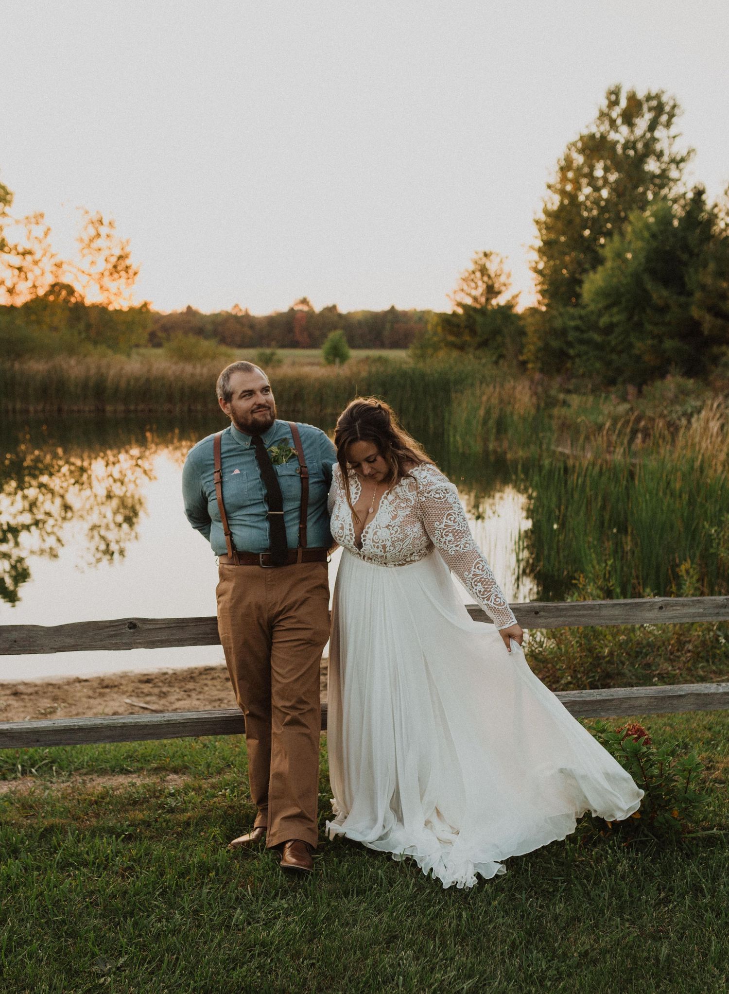 A couple shares a romantic moment on grass near a lake during golden hour.