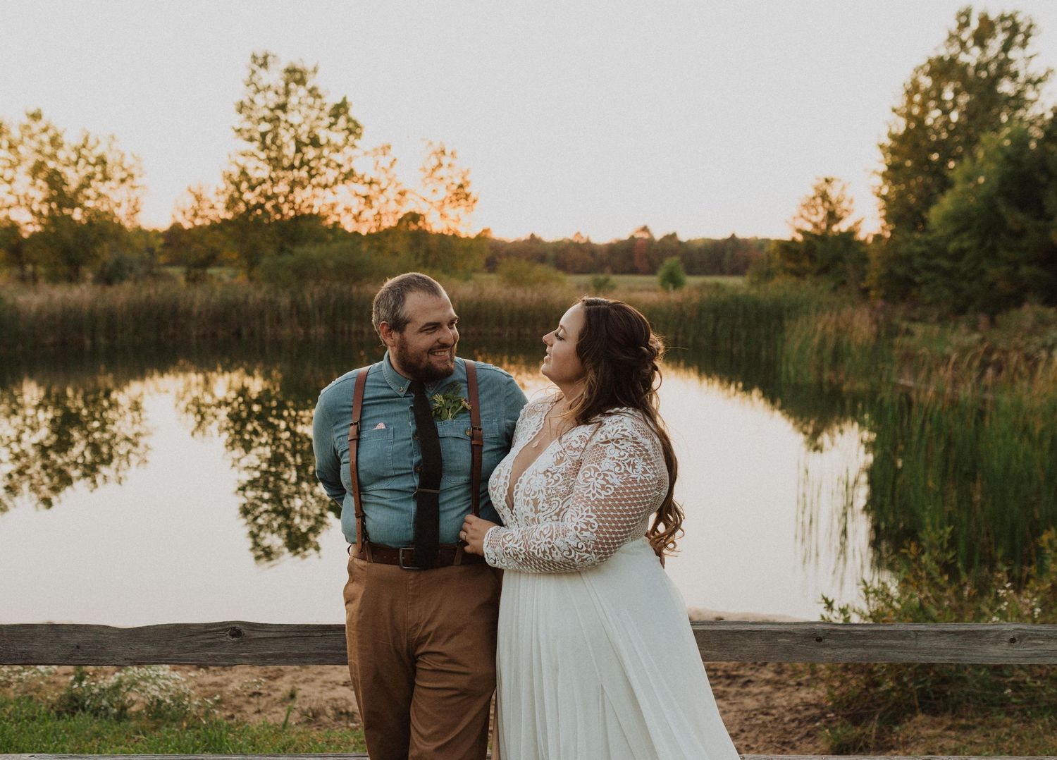 A couple embraces by a serene lake during sunset with natural landscape in background.