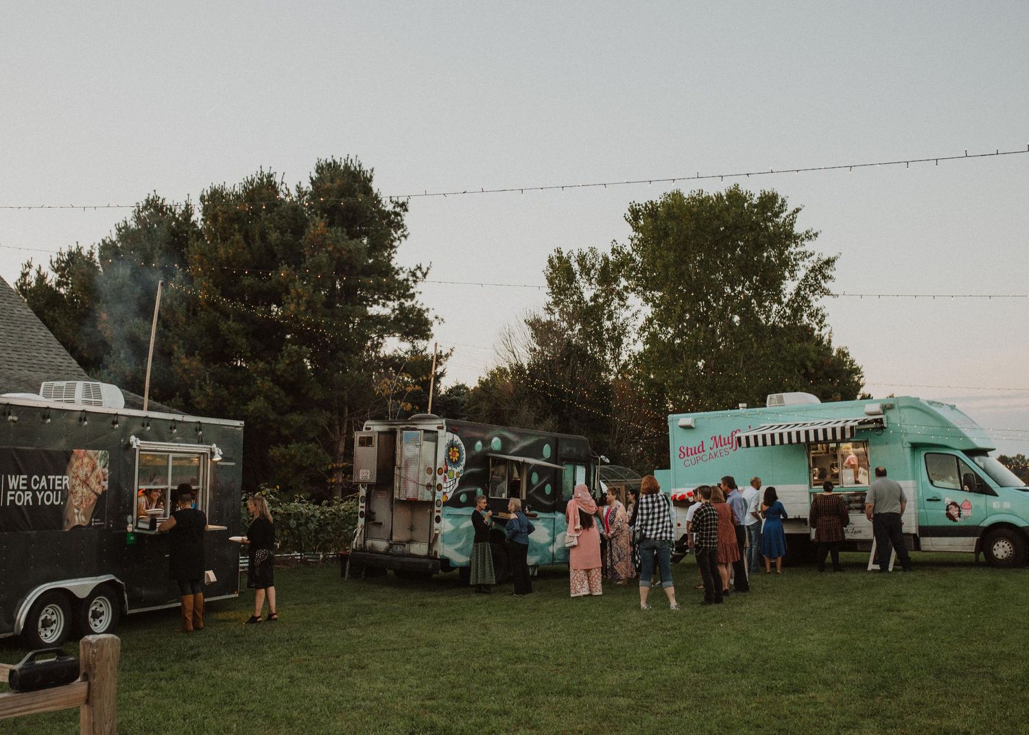 A casual outdoor gathering with food trucks and guests enjoying the evening.