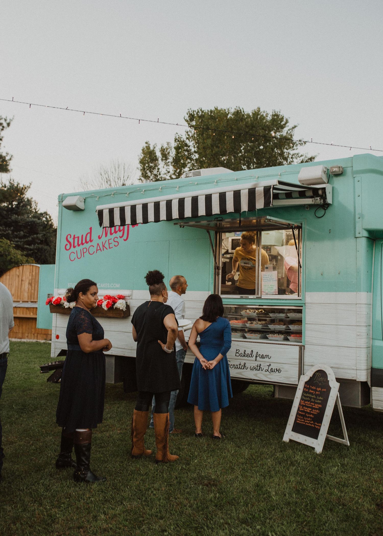 A mint green vintage food truck serving guests at an outdoor event.