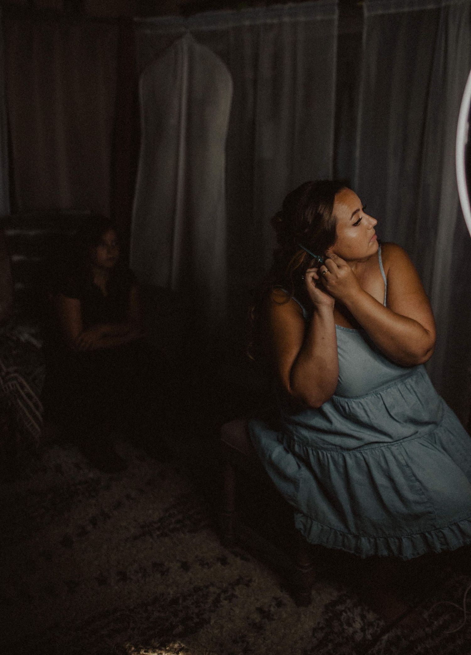 Person in a blue dress sits in a dimly lit room while getting ready.