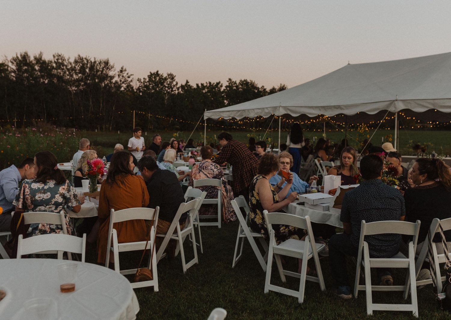 Wedding guests seated at tables under a white tent during an outdoor evening celebration.
