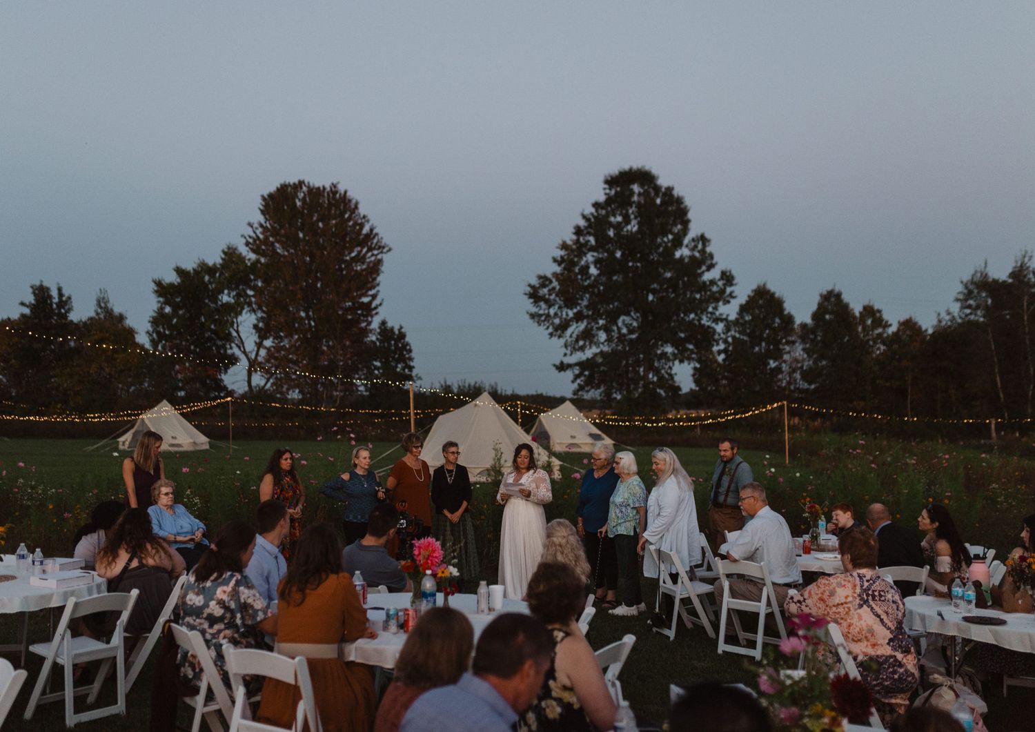 Evening outdoor wedding reception with guests dining under string lights.