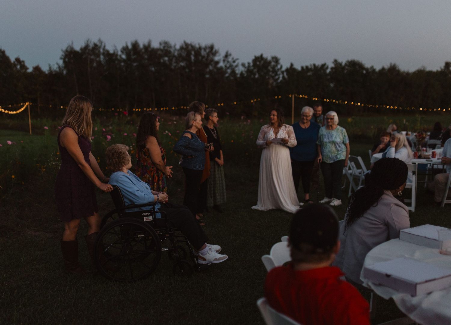 Twilight wedding reception scene with string lights and guests seated at outdoor tables.