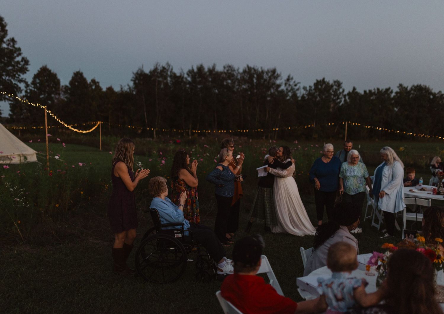 Outdoor wedding celebration at dusk with string lights illuminating the reception area.