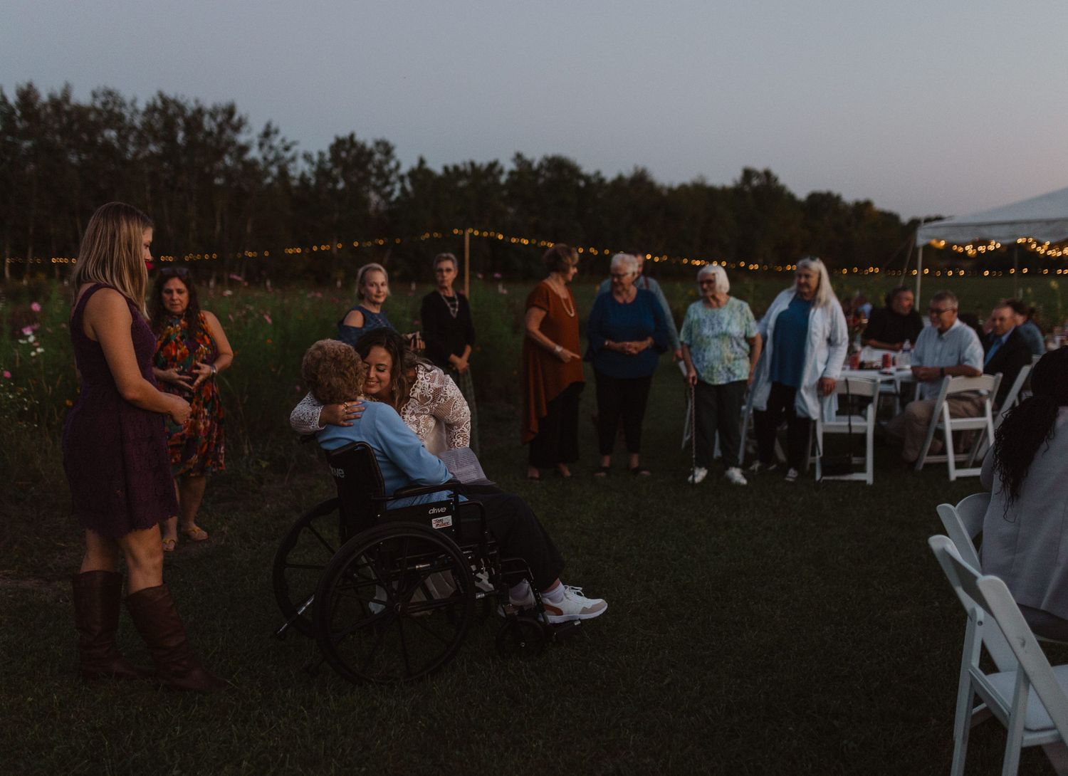 An outdoor evening gathering with string lights and guests mingling on a grassy lawn.