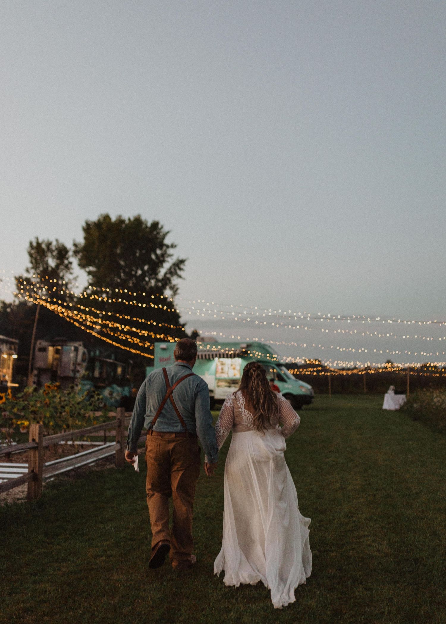 A couple walks through an outdoor evening event with string lights hanging overhead in a romantic setting.