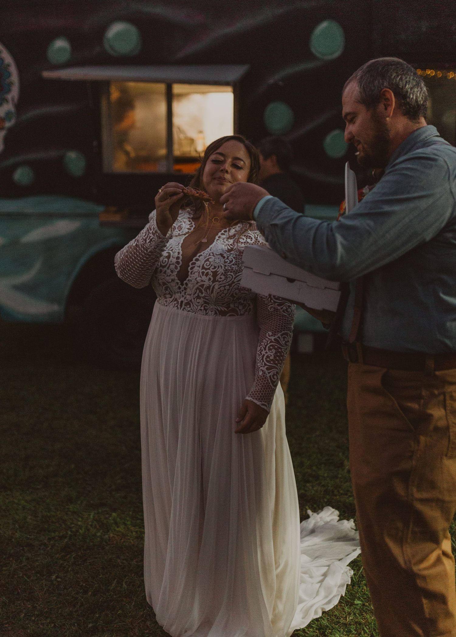 A couple shares a moment together near food trucks at an evening outdoor celebration.