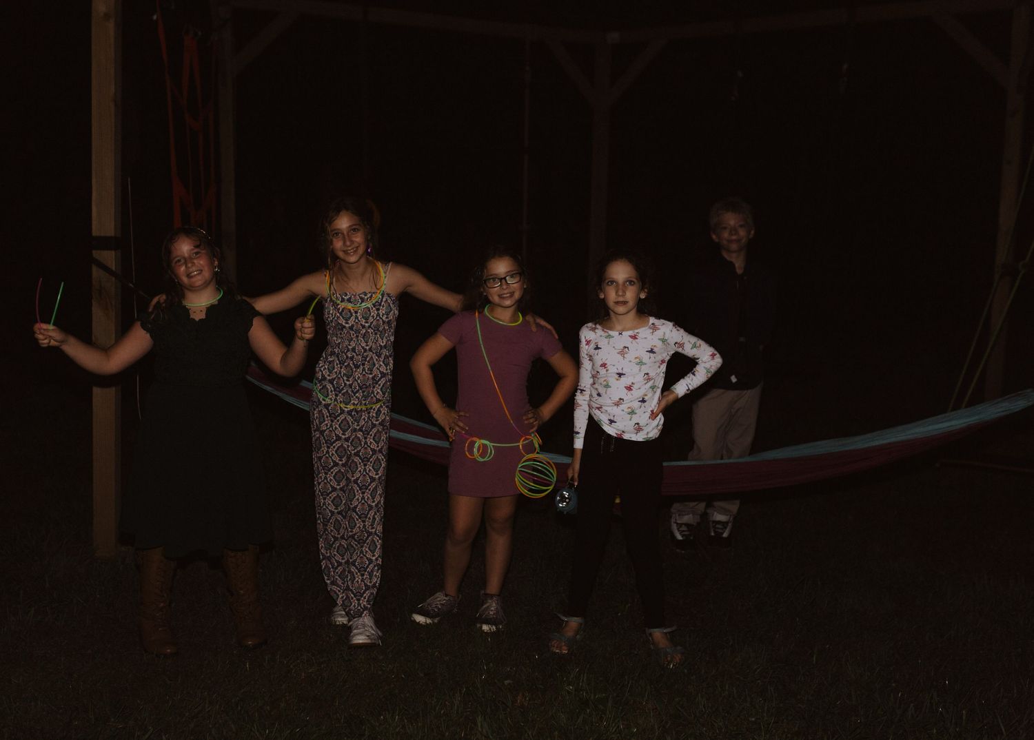 Party guests play outdoor games in the dark with string lights twinkling above.