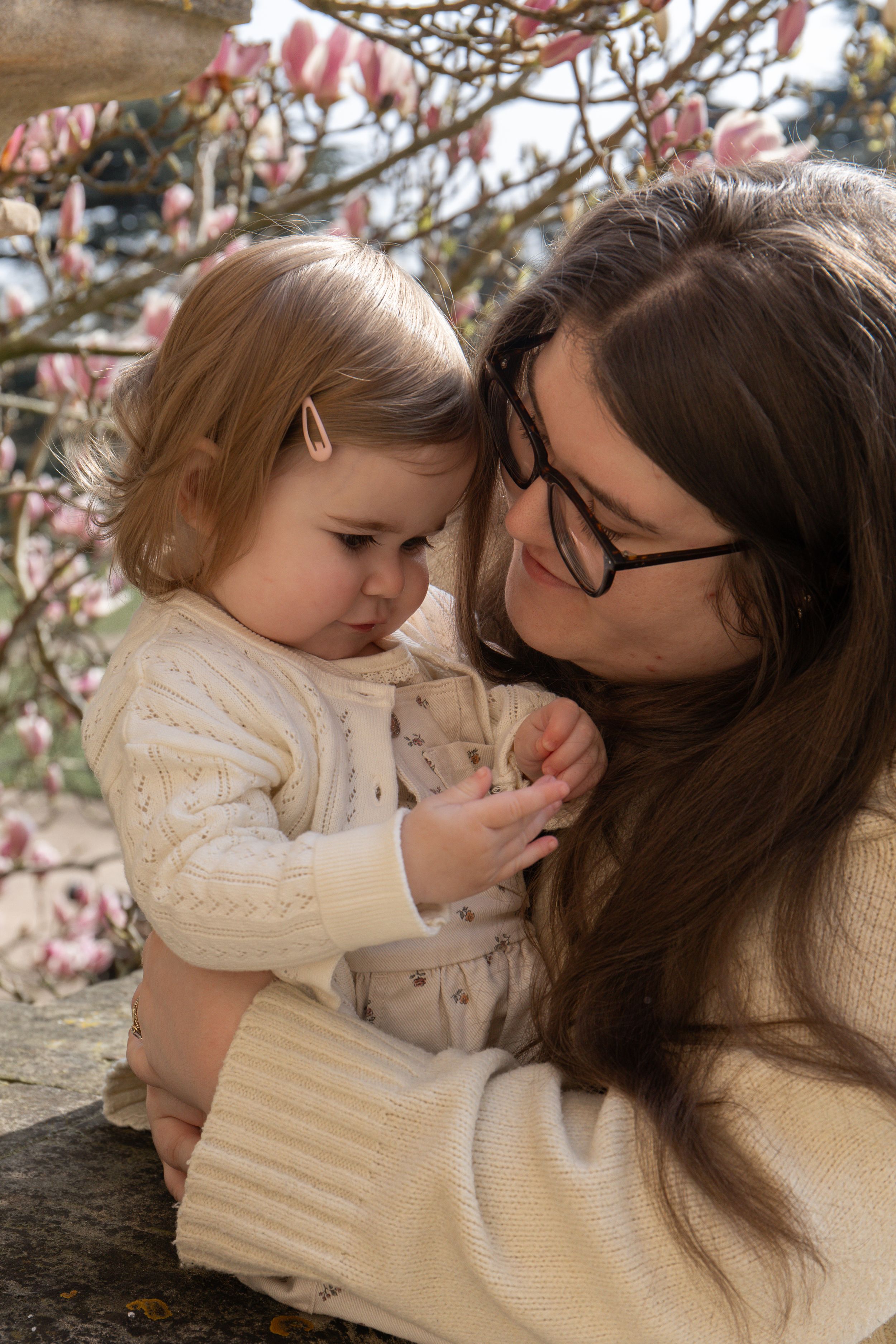 A mother holding her toddler daughter near blooming magnolia tree, family photoshoot Nottingham park session