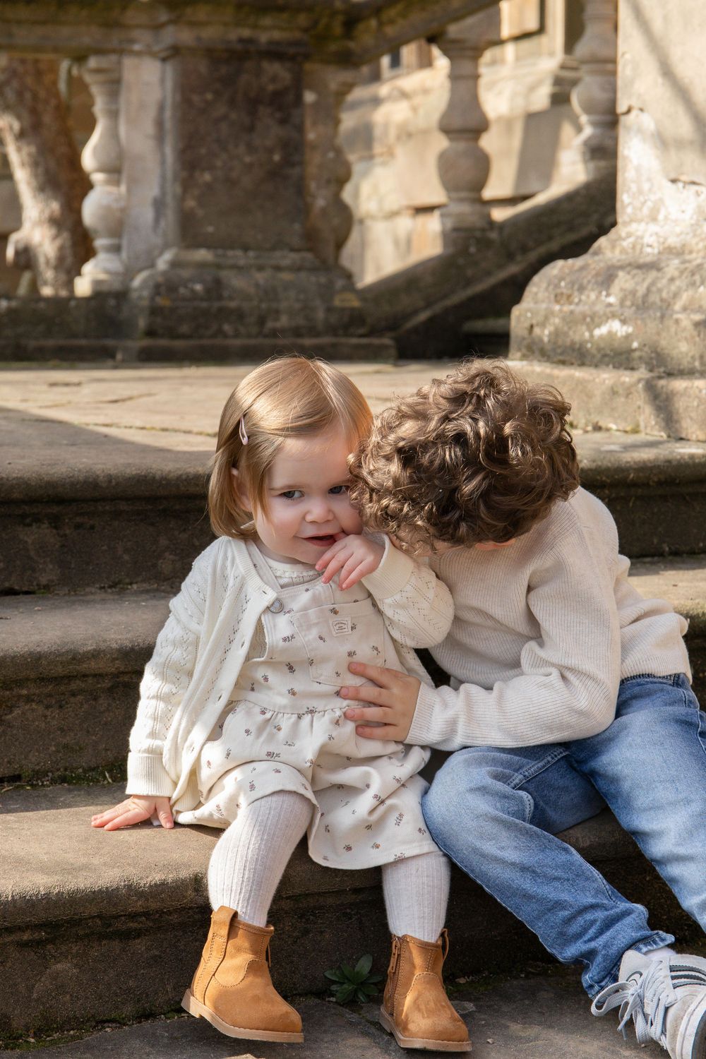 Two young children in cream outfits sit on stone steps, Family outdoor photoshoot Nottingham