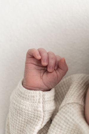 Close-up of a newborn baby's tiny clenched fist in a cream knit outfit against a white background relaxed newborn photoshoot Nottingham