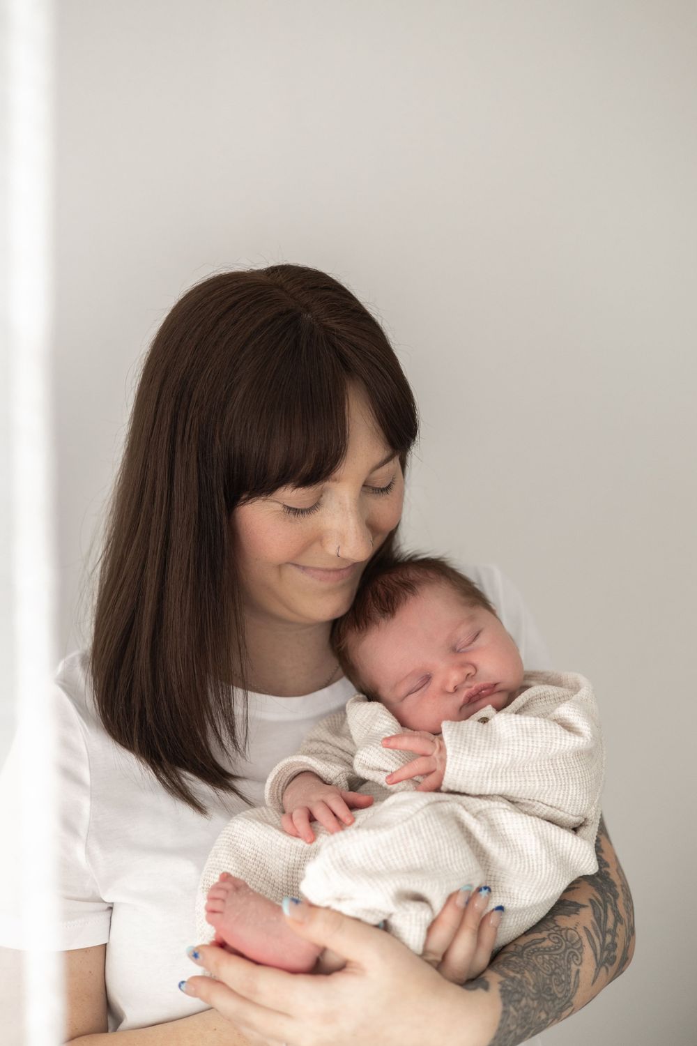 A smiling mother holds her sleeping newborn baby dressed in a white outfit natural newborn photography Nottingham NG16