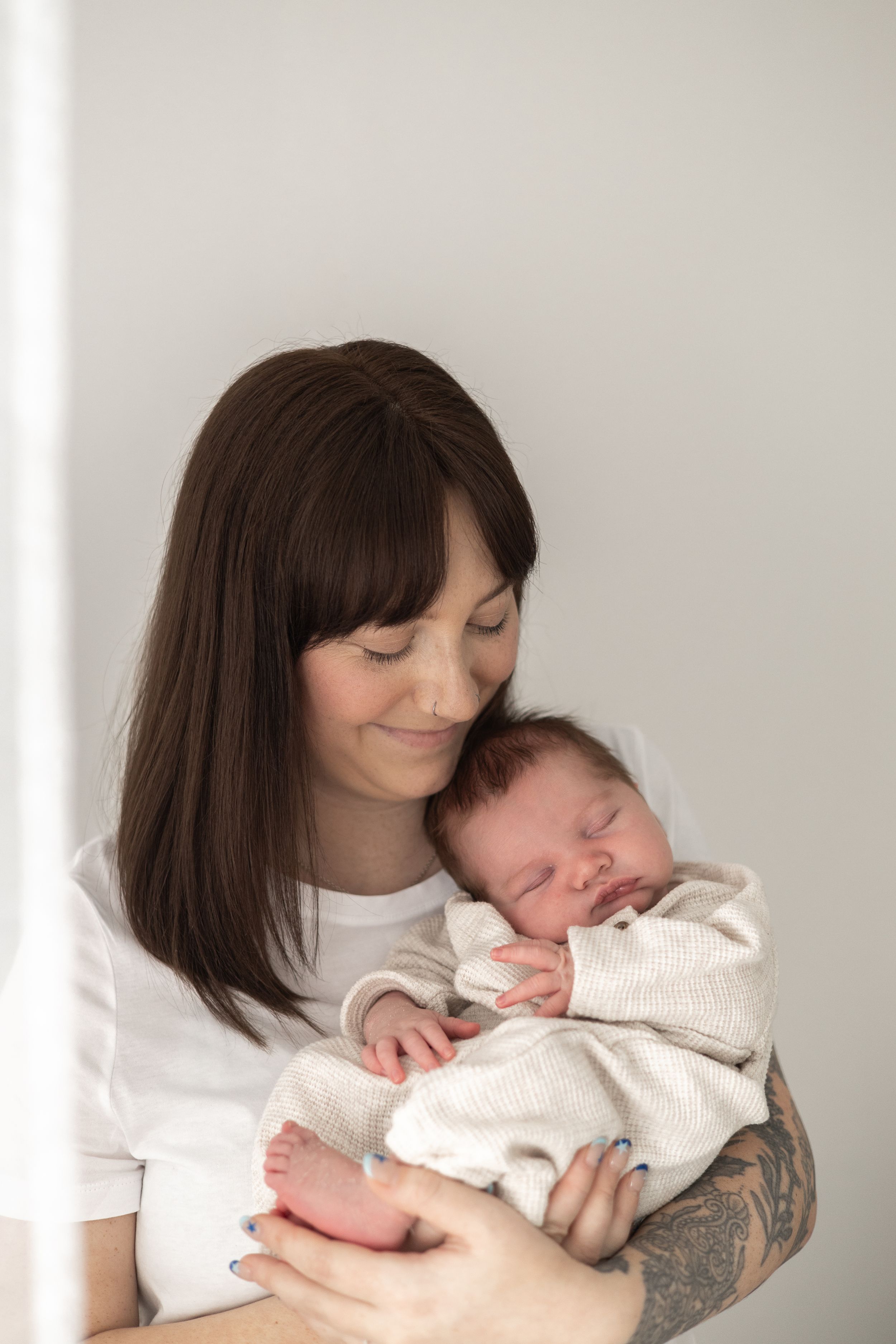 A smiling mother holds her sleeping newborn baby dressed in a white outfit natural newborn photography Nottingham NG16