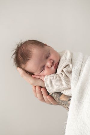 Sleeping newborn baby cradled in adult hands, wrapped in a soft cream knit blanket, relaxed newborn photoshoot Nottingham