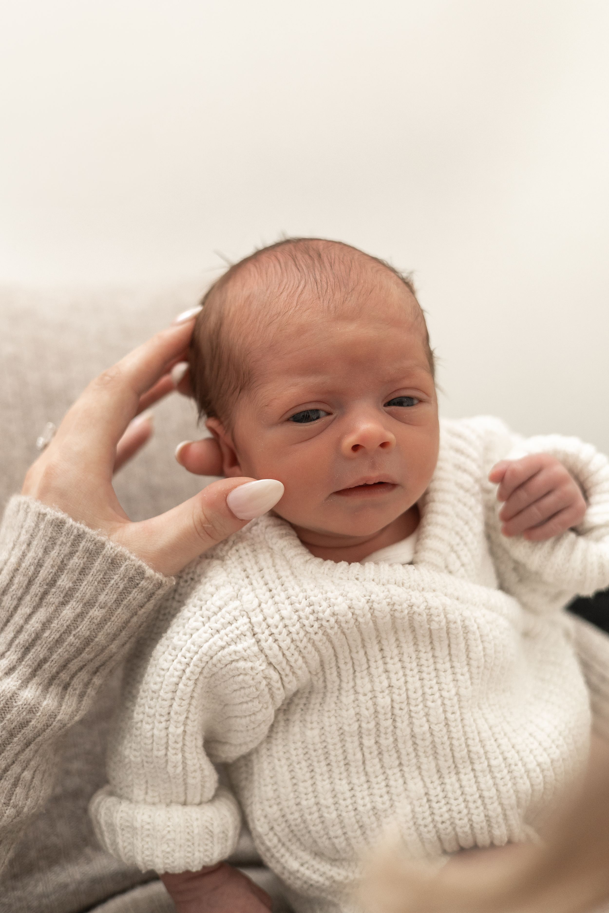 Newborn baby in white knit sweater being cradled by a parent's hand Nottingham NG16 natural newborn photography