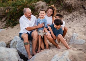 A joyful family shares a candid moment while sitting on rocks at the beach.