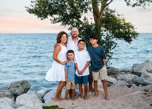 A family group poses together on rocky shoreline during sunset by the ocean.