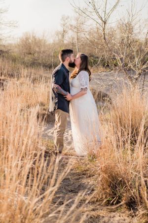 A couple shares a romantic moment in tall golden grass during sunset.