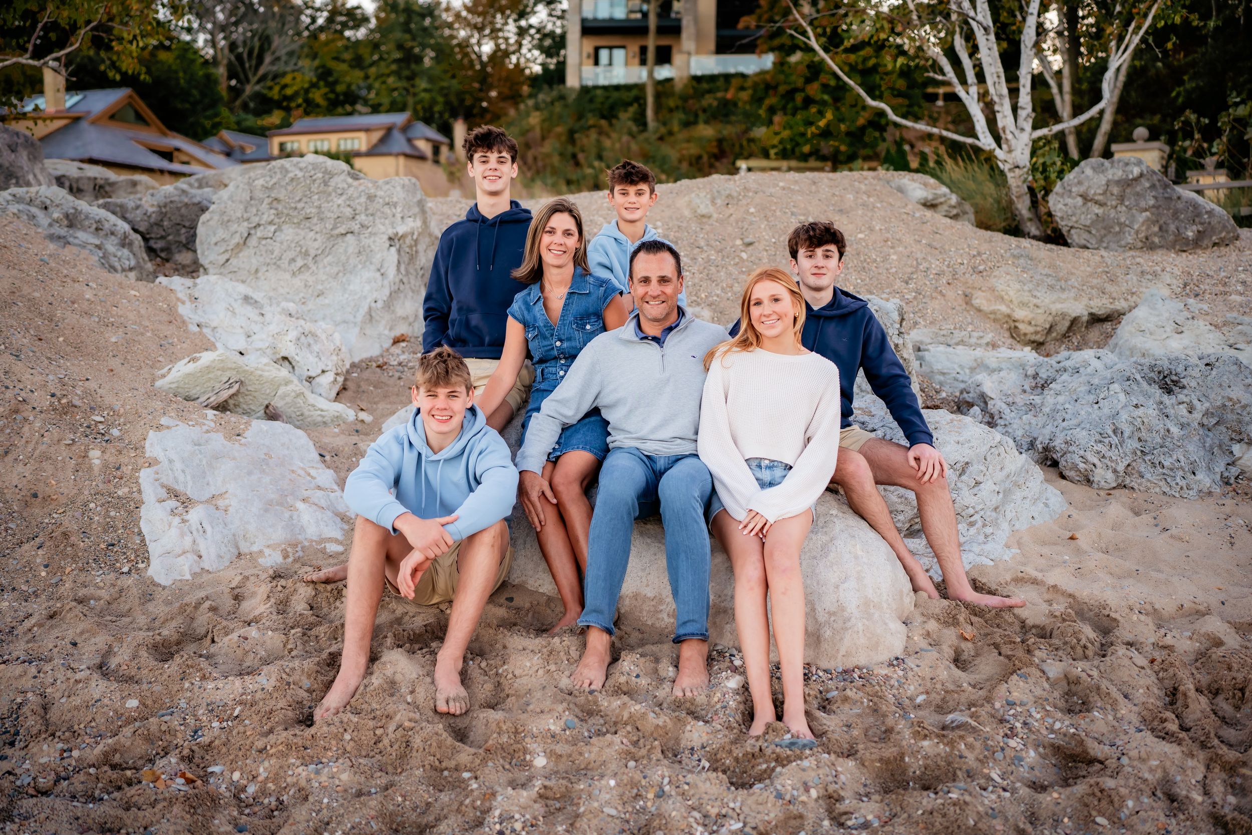 Family of six enjoying the sunset on the beach, with children playing in the sand, and parents holding hands, smiling.