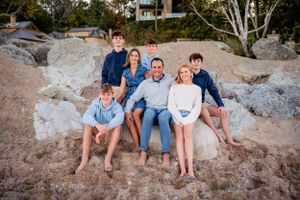 Family of six enjoying the sunset on the beach, with children playing in the sand, and parents holding hands, smiling.
