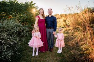 A family poses together outdoors with two children wearing matching pink tulle dresses.