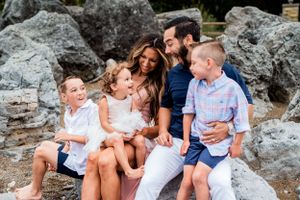 A family shares a happy moment while sitting together on coastal rocks.