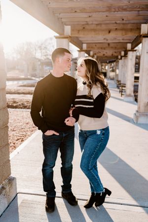 A couple shares an intimate moment under a covered walkway with sunlight streaming in.