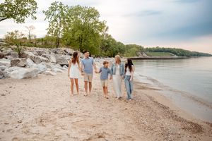Group walking together on a rocky beach shoreline by the water during sunset with trees in the background.