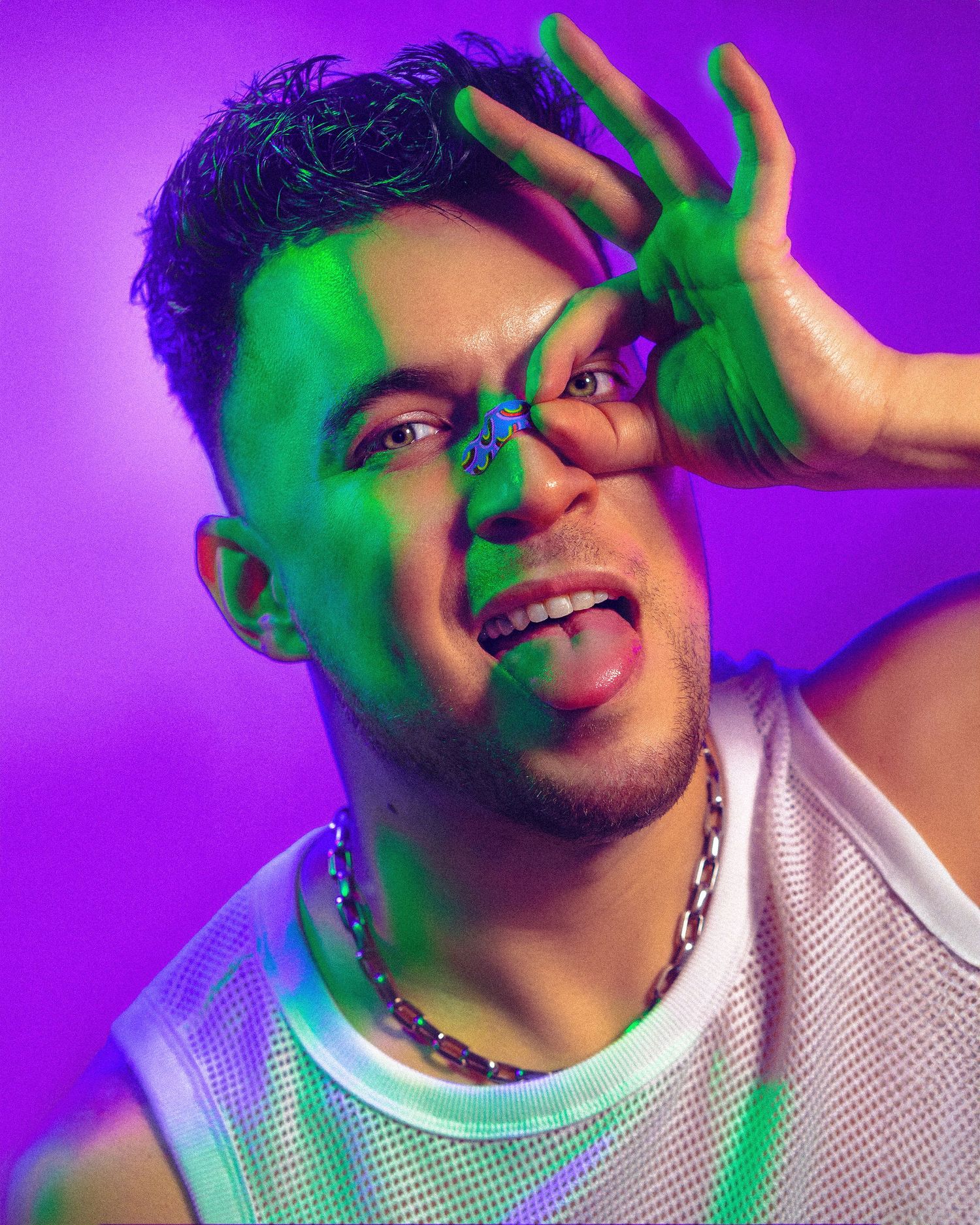 Colorful portrait with green lighting effects and purple background showing playful expression.