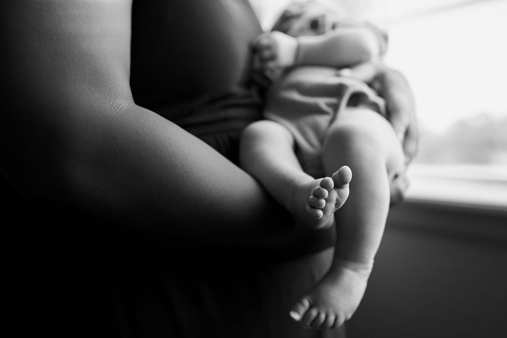 Black and white image of a baby lay in mothers arms, the focus is on baby's foot and mothers arms