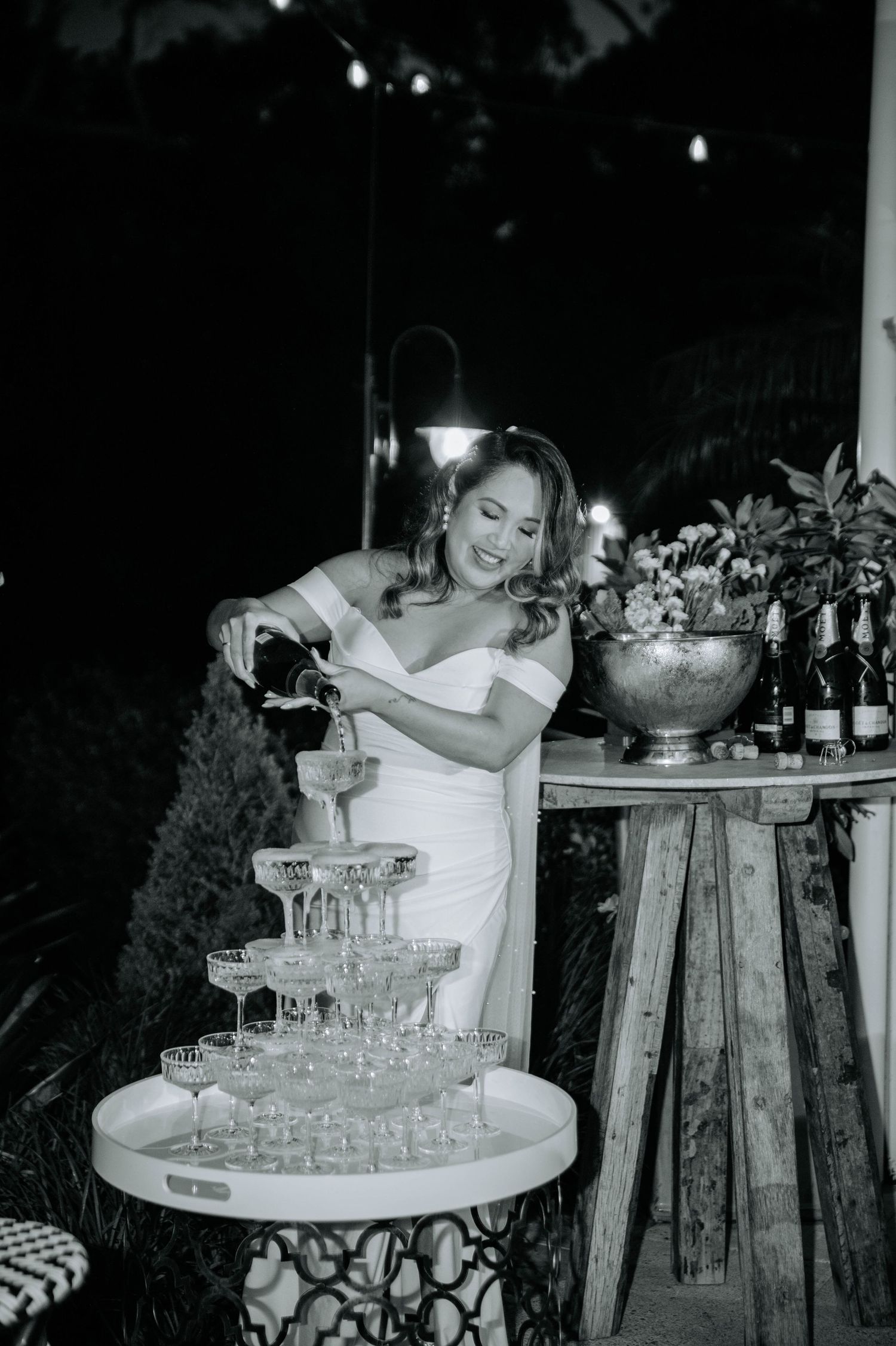 Pouring champagne into a tower of glasses at an evening wedding reception.